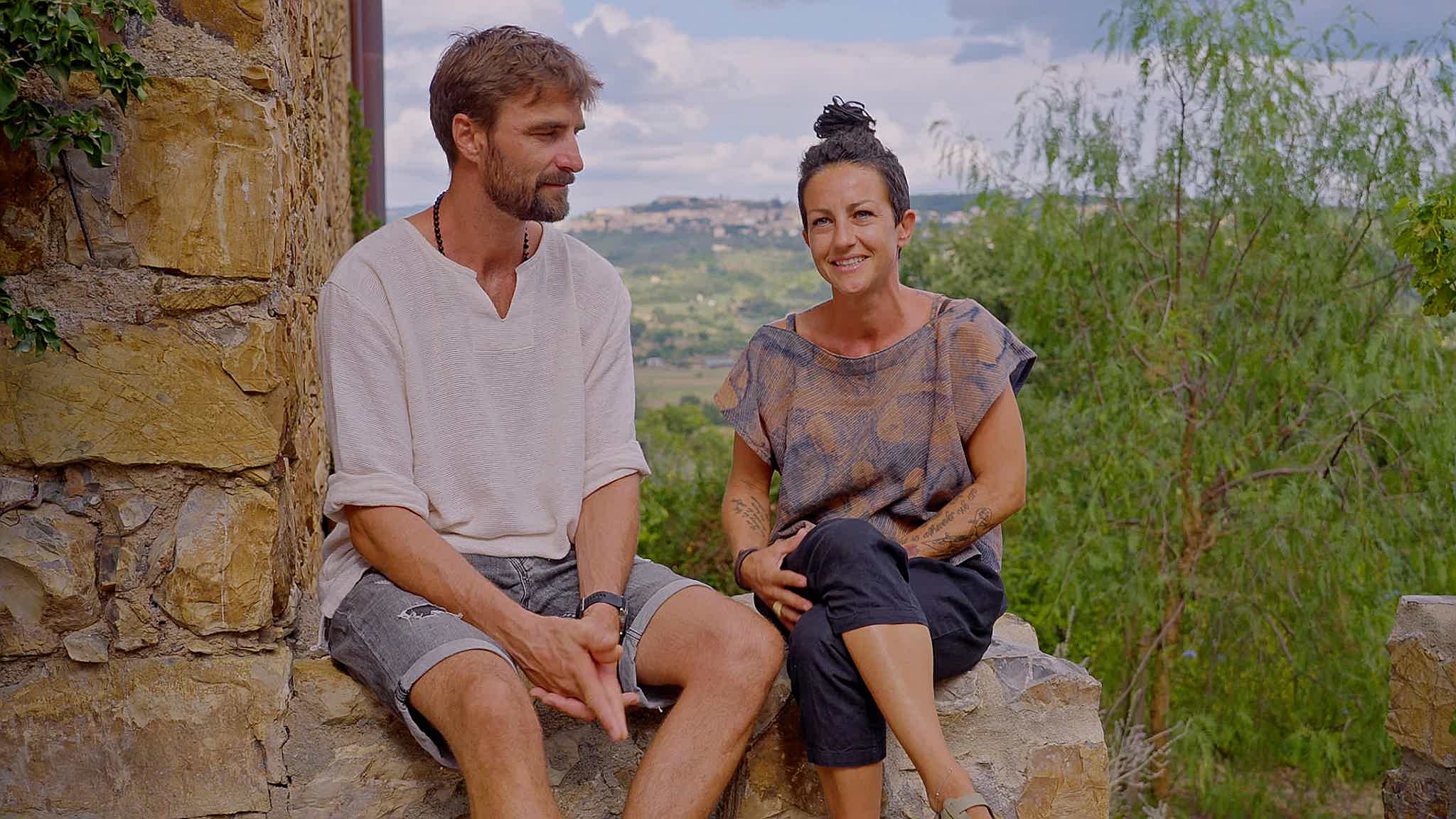 Mario and Cecilia at their guesthouse Schiaccia Ghiande, smiling with a view of Tuscany's Massa Marittima hills.