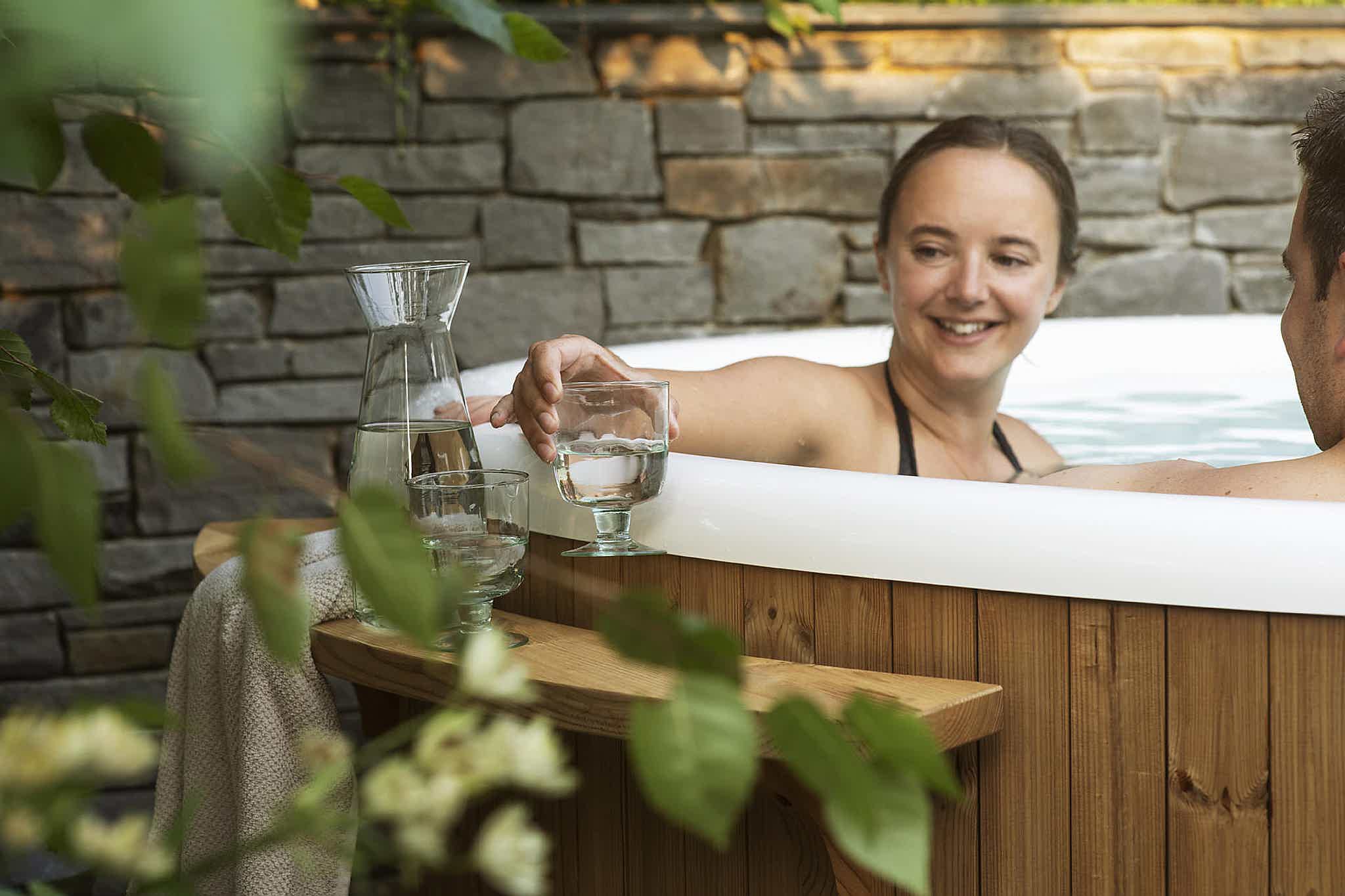 Victoria relaxes with her husband in a Skargards Regal hot tub, surrounded by nature, enjoying drinks.