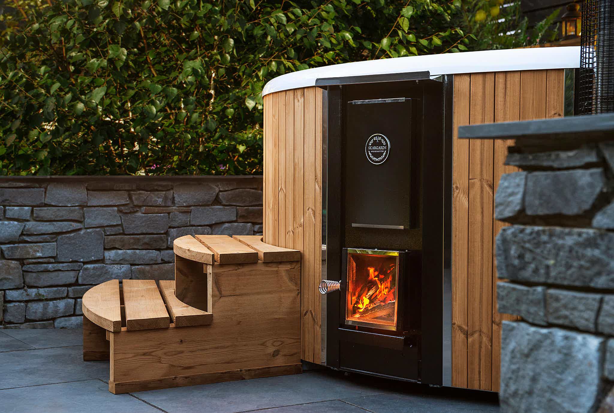 Skargards Regal DualBurn hot tub with a lit stove in a garden setting.