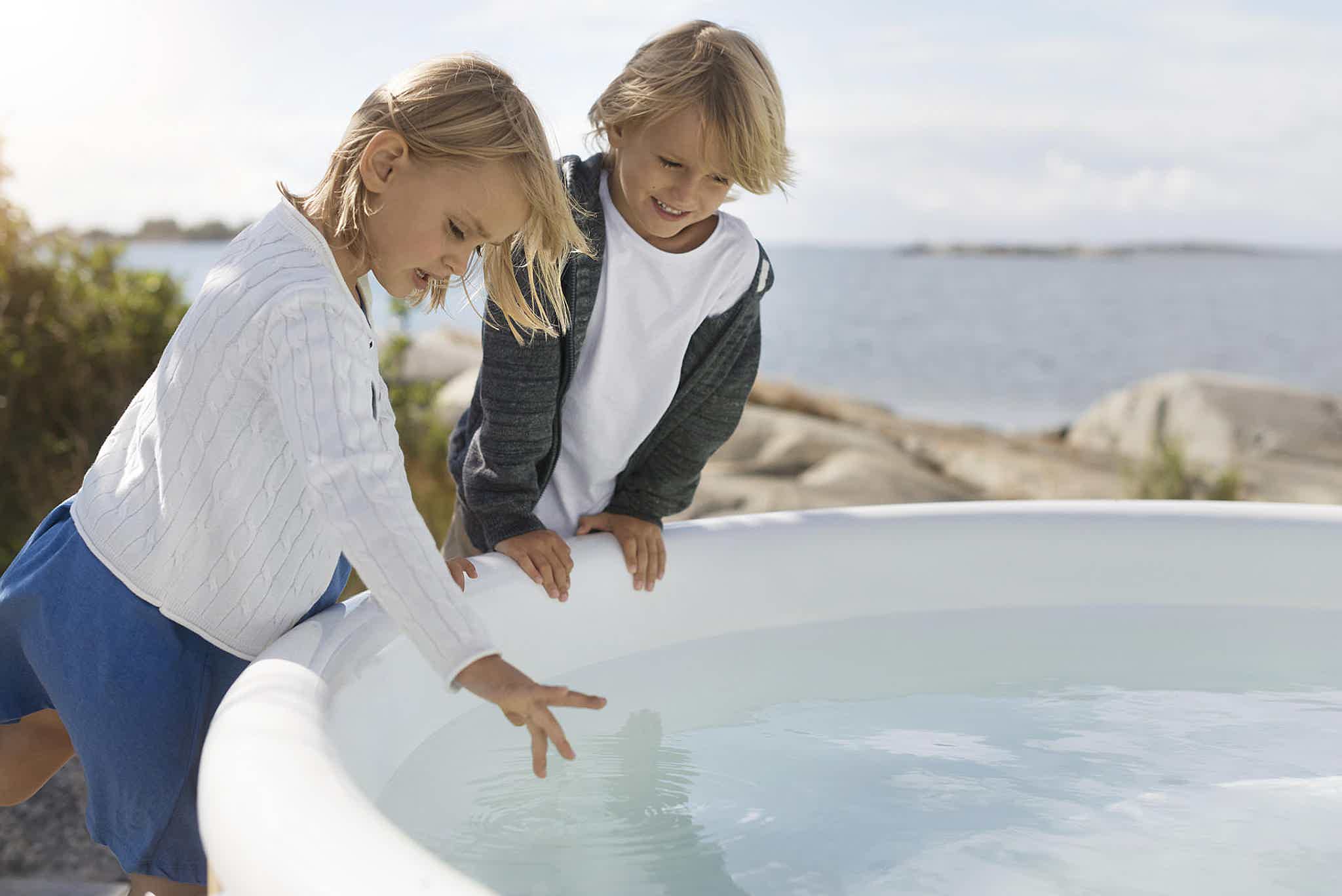 Two children playing near a Skargards Hot Tubs Regal with a scenic island backdrop.