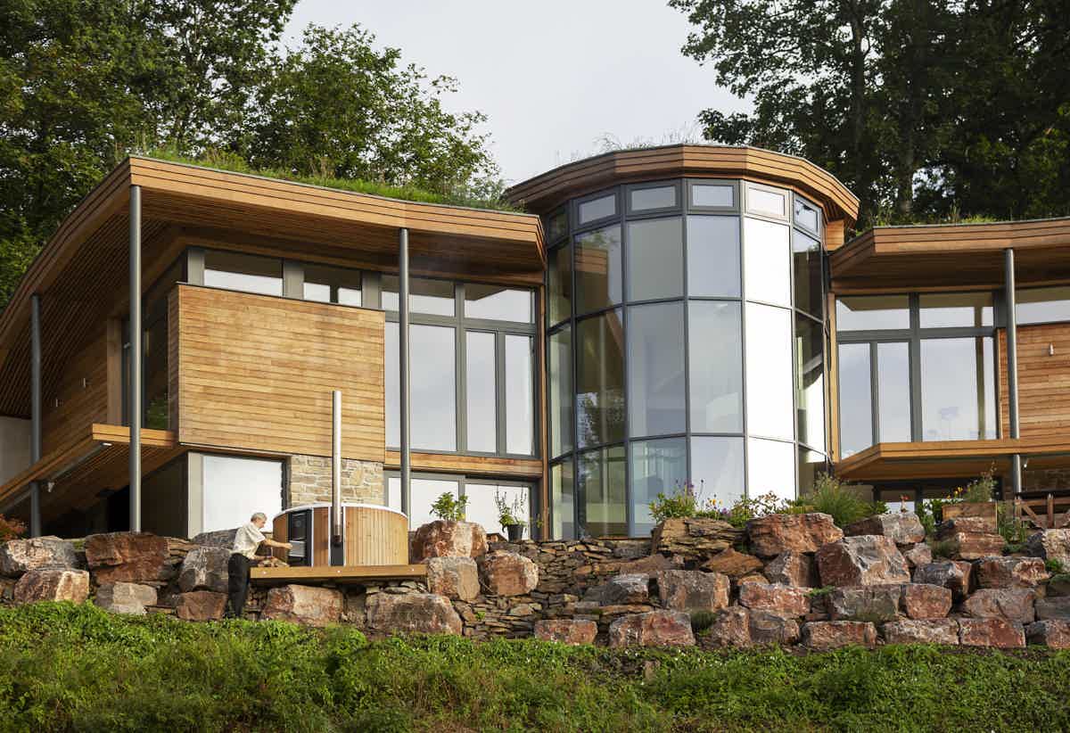 A wooden house with large windows and a stone wall. A Skargards Regal DualBurn 190 hot tub is on the terrace.