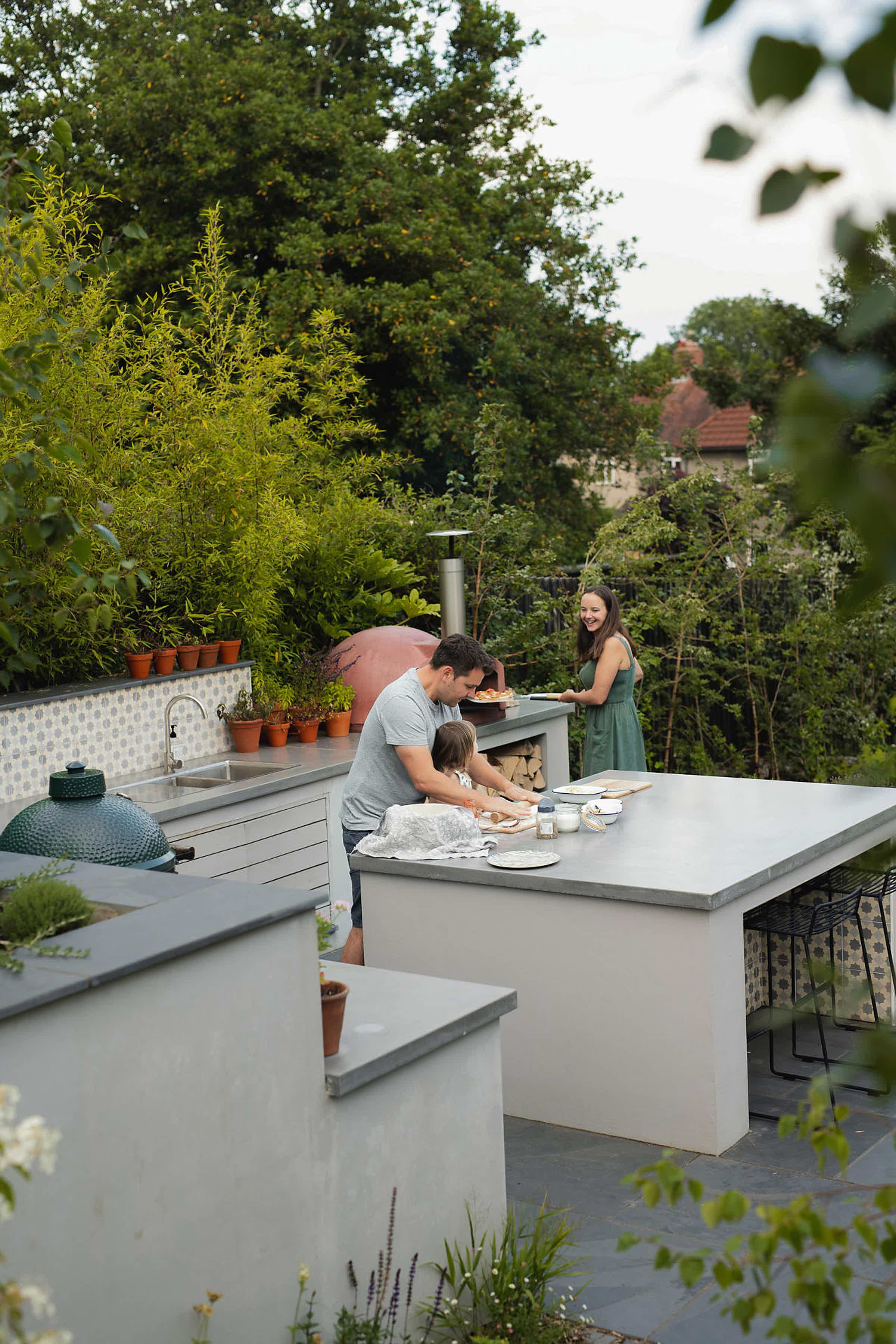 Victoria and her family cooking in their outdoor kitchen, surrounded by lush greenery.