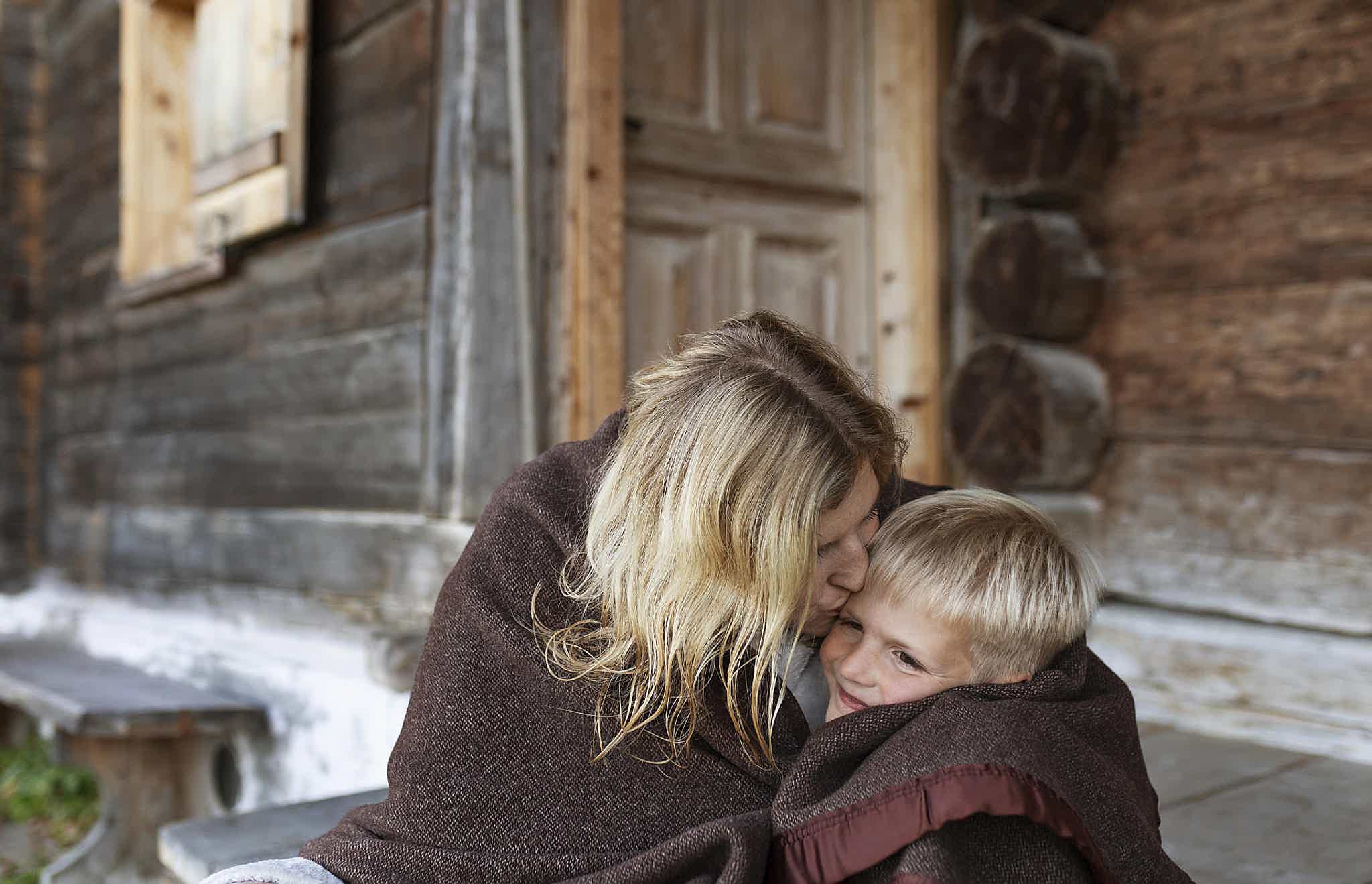 Nicole and her son wrapped in a blanket outside their wooden cabin.