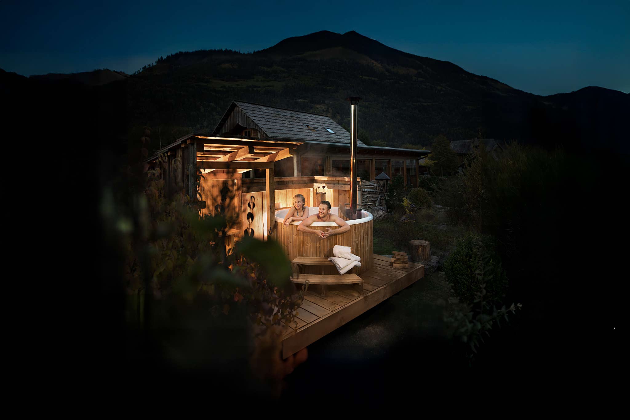 Three people enjoying a luxurious hot tub on a wooden deck with a mountain view.