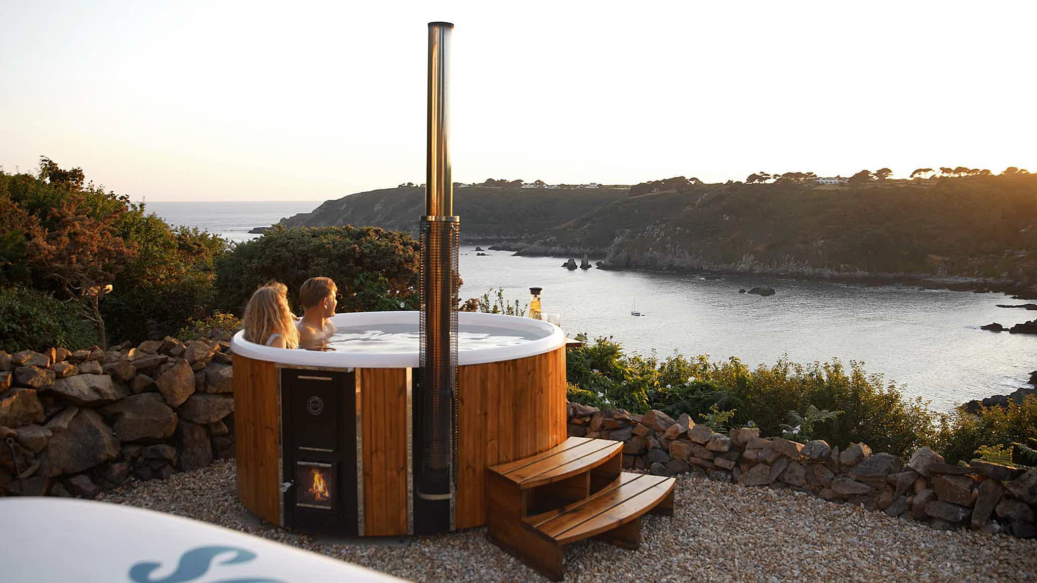 A couple in a Skargards Regal hot tub by the ocean, watching the sunset.