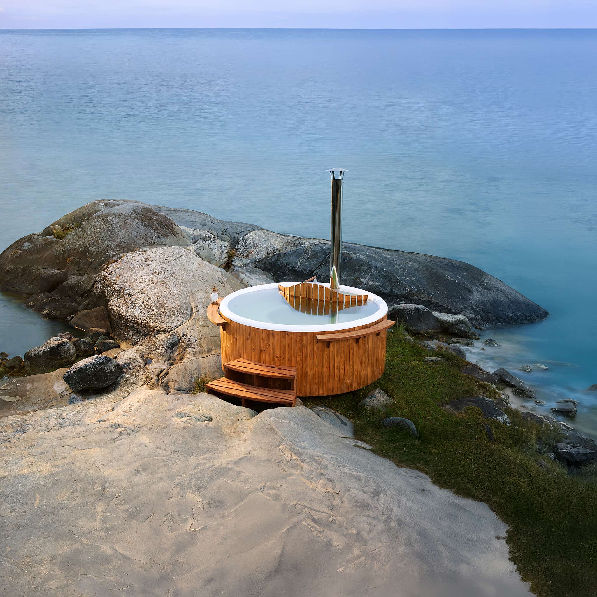 A wooden hot tub on a rocky shore with calm water and a tall metal pole, creating a tranquil scene.
