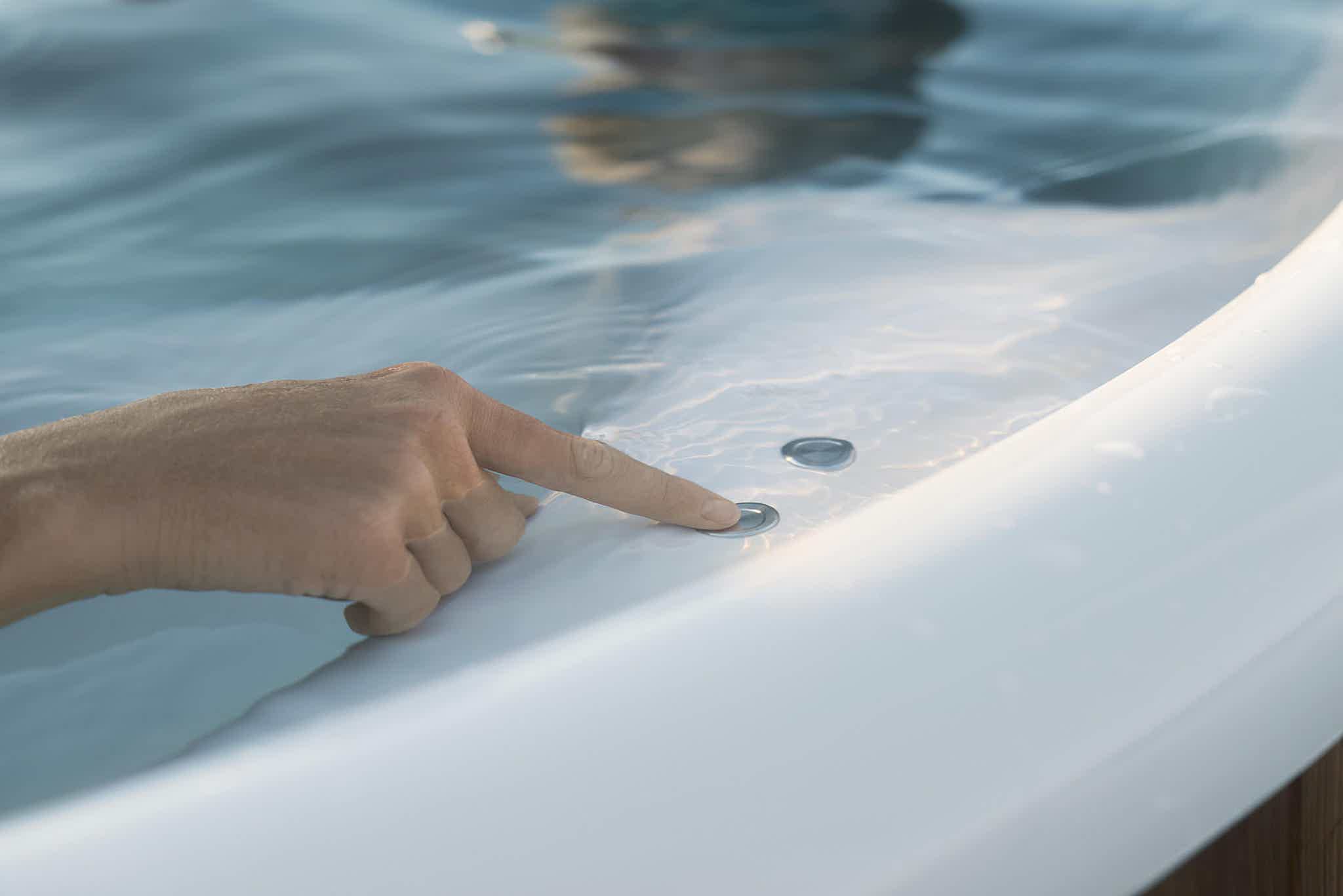 A hand reaches into a white hot tub with a silver coin on the edge.