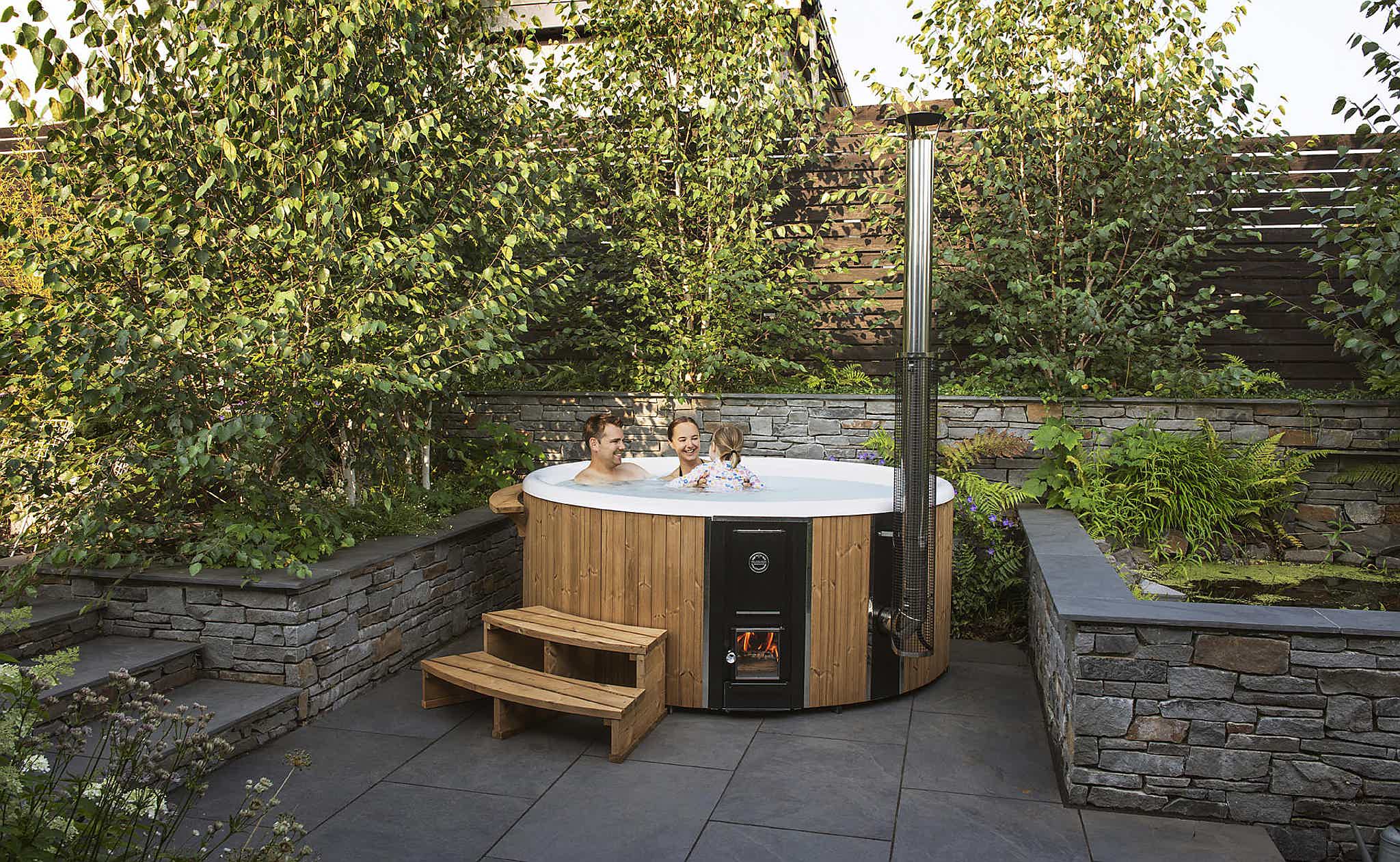A Skargards Regal DualBurn 220 hot tub on a stone terrace with Victoria and her family, surrounded by greenery.