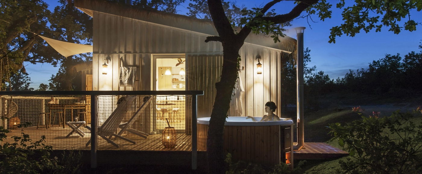 Shot of a woman sitting in the Regal hot tub enjoying the evening. In the background is a luxury tree house.