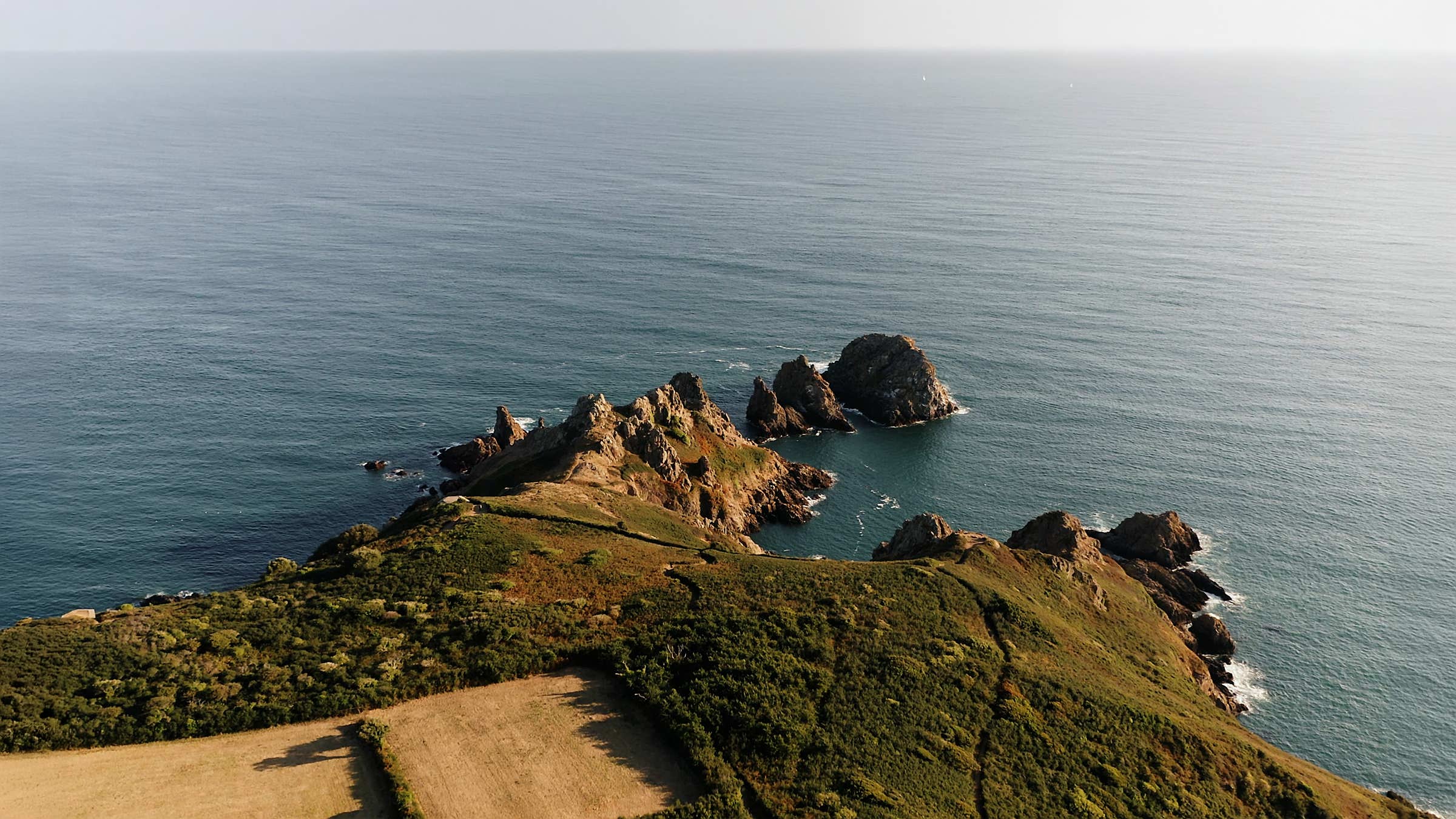 Aerial view of a coastline with grassy hills and vast waters.