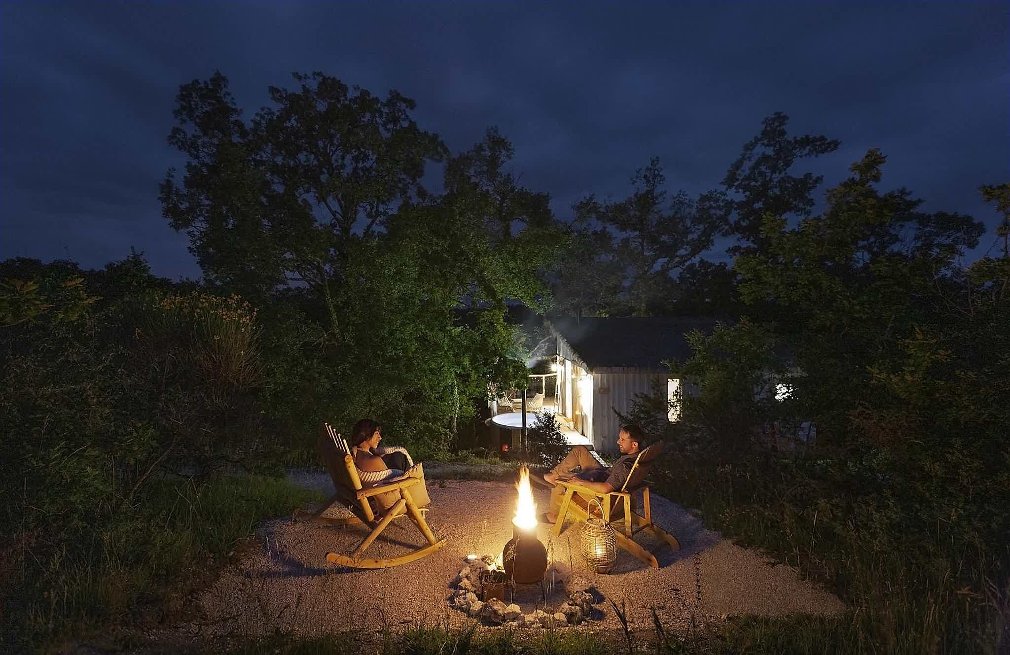 A couple enjoys a bonfire with a wood-fired Skargards Regal hot tub in the background.