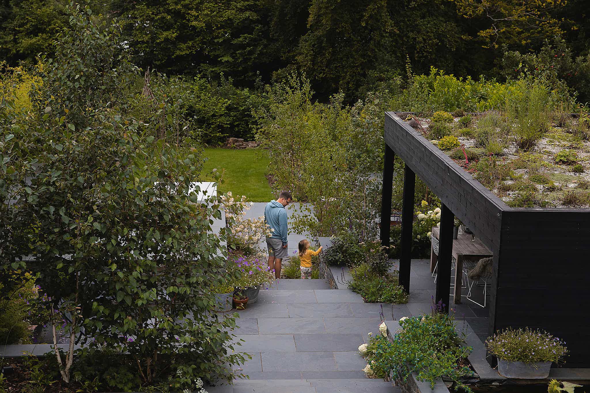 A garden with a black wooden seating area and green roof. A family enjoys the lush scenery.