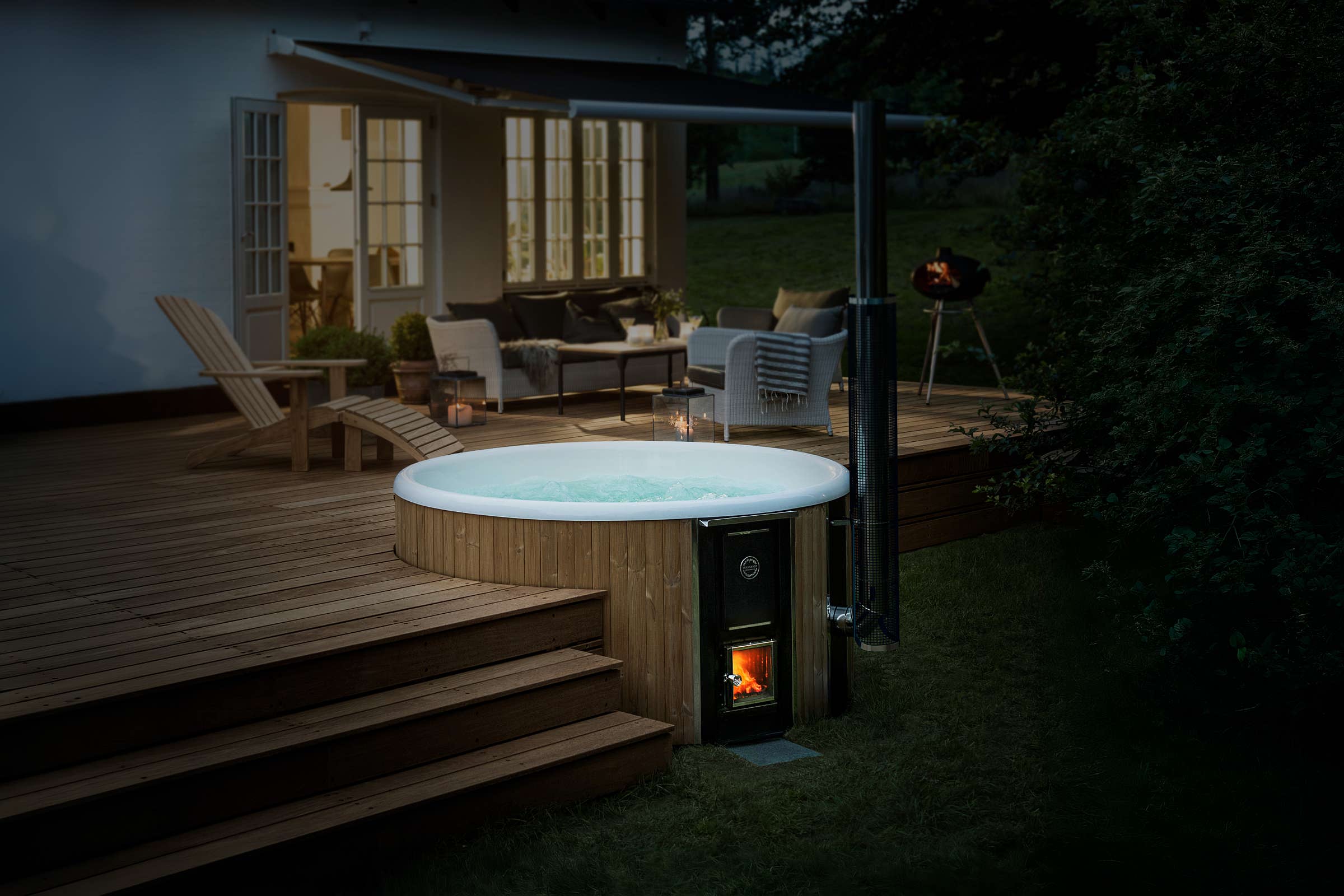 Wooden deck with a hot tub, couch, table, grill, and fire pit, surrounded by a fence.