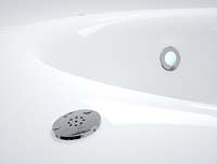 A modern bathroom with a white bathtub featuring a circular drain and water outlet, surrounded by white walls.