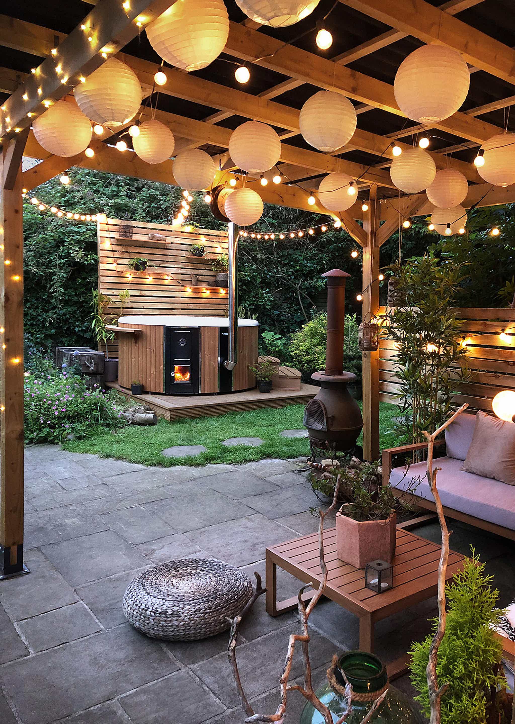 A cozy outdoor patio with a wooden pergola, lights, plants, and a Skargards hot tub in the background.