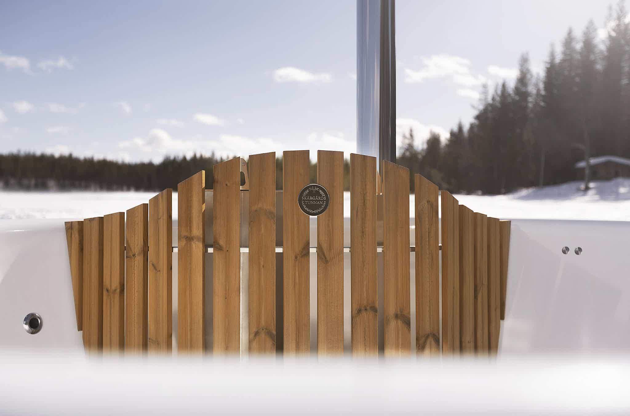 A luxurious hot tub with a wooden fence and a window overlooking a snowy landscape.