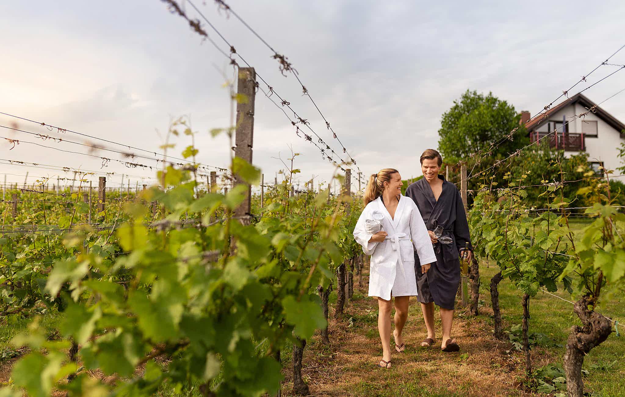 Frauke and Markus in the vineyard behind their house, both wearing bathrobes, smiling at each other.