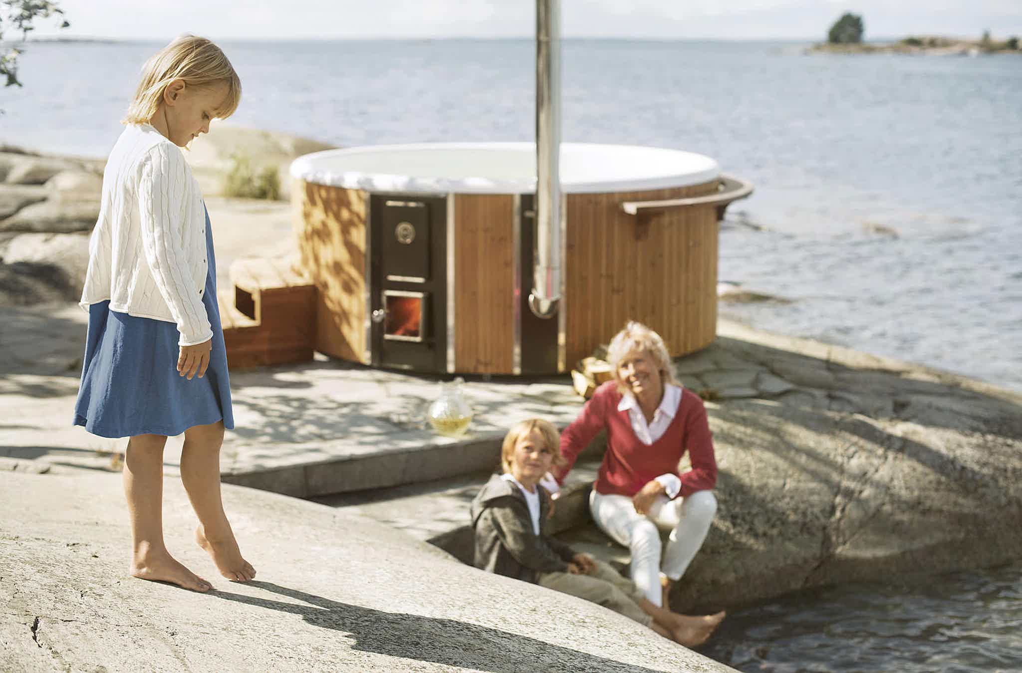 A grandmother and her grandchildren enjoying a Skargards Regal hot tub by the rocky shore.