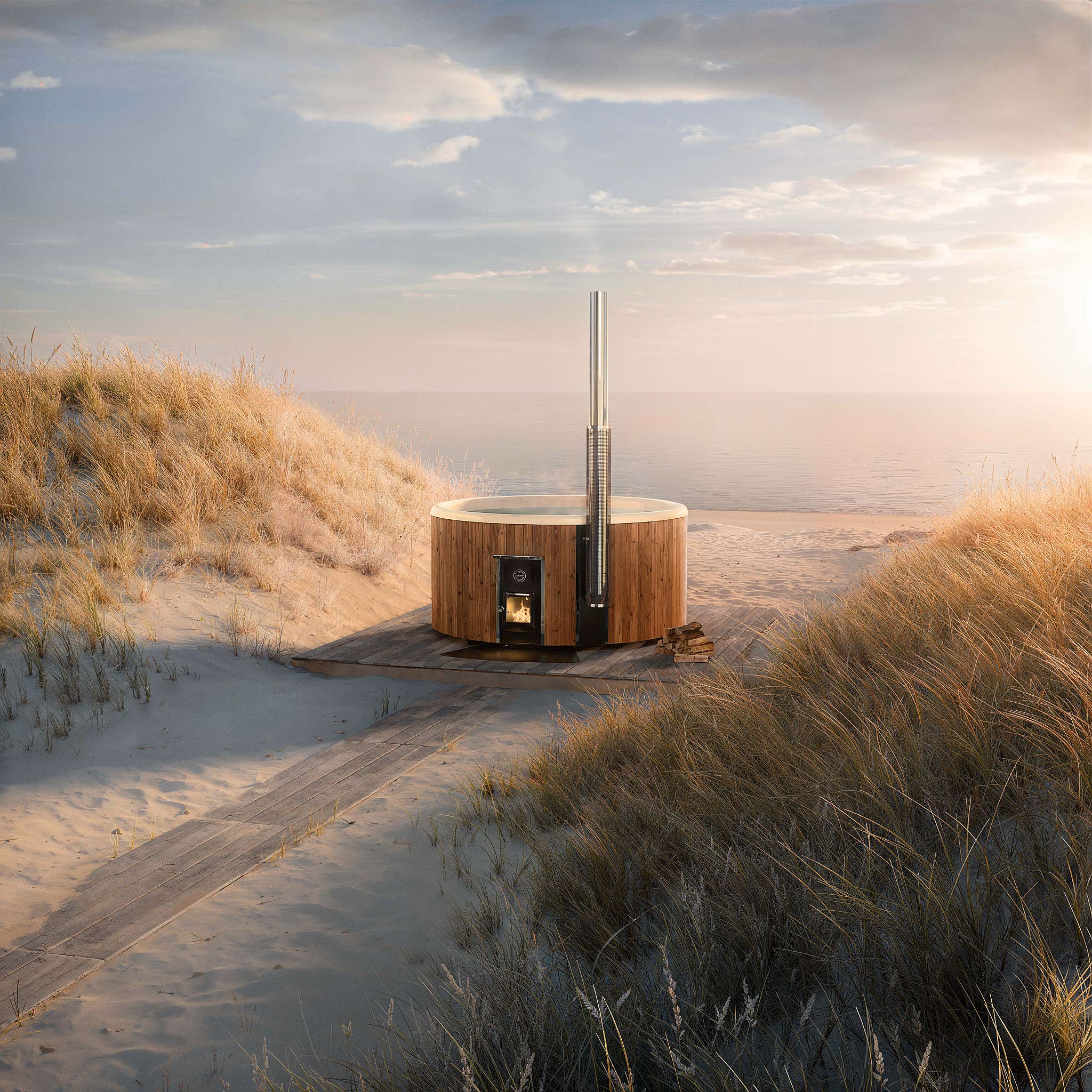 A circular wooden hot tub on a sandy beach with a fire inside, surrounded by tall grasses.
