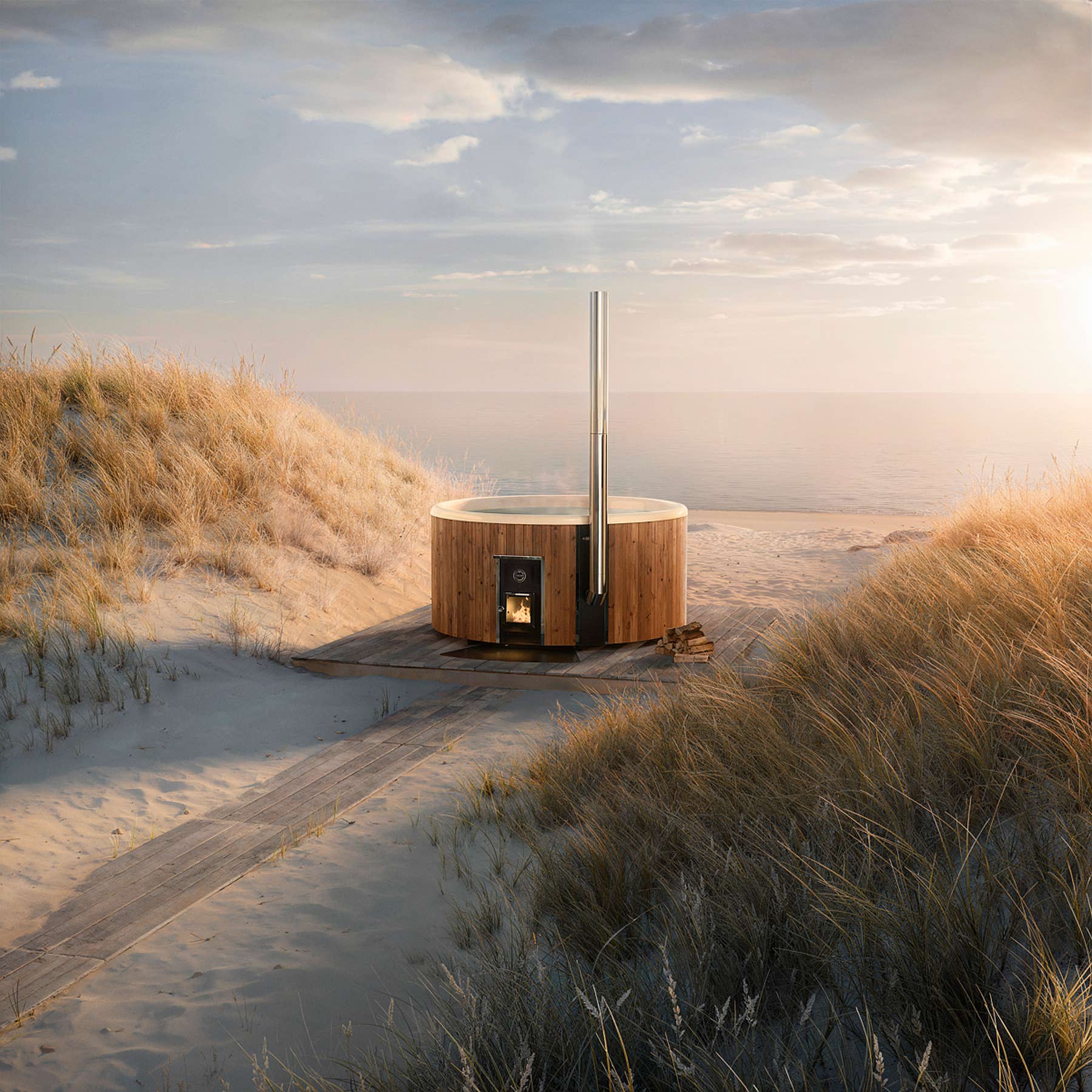 A wooden hot tub on a sandy beach with tall grasses and a path. The sunset casts a warm glow over the scene.