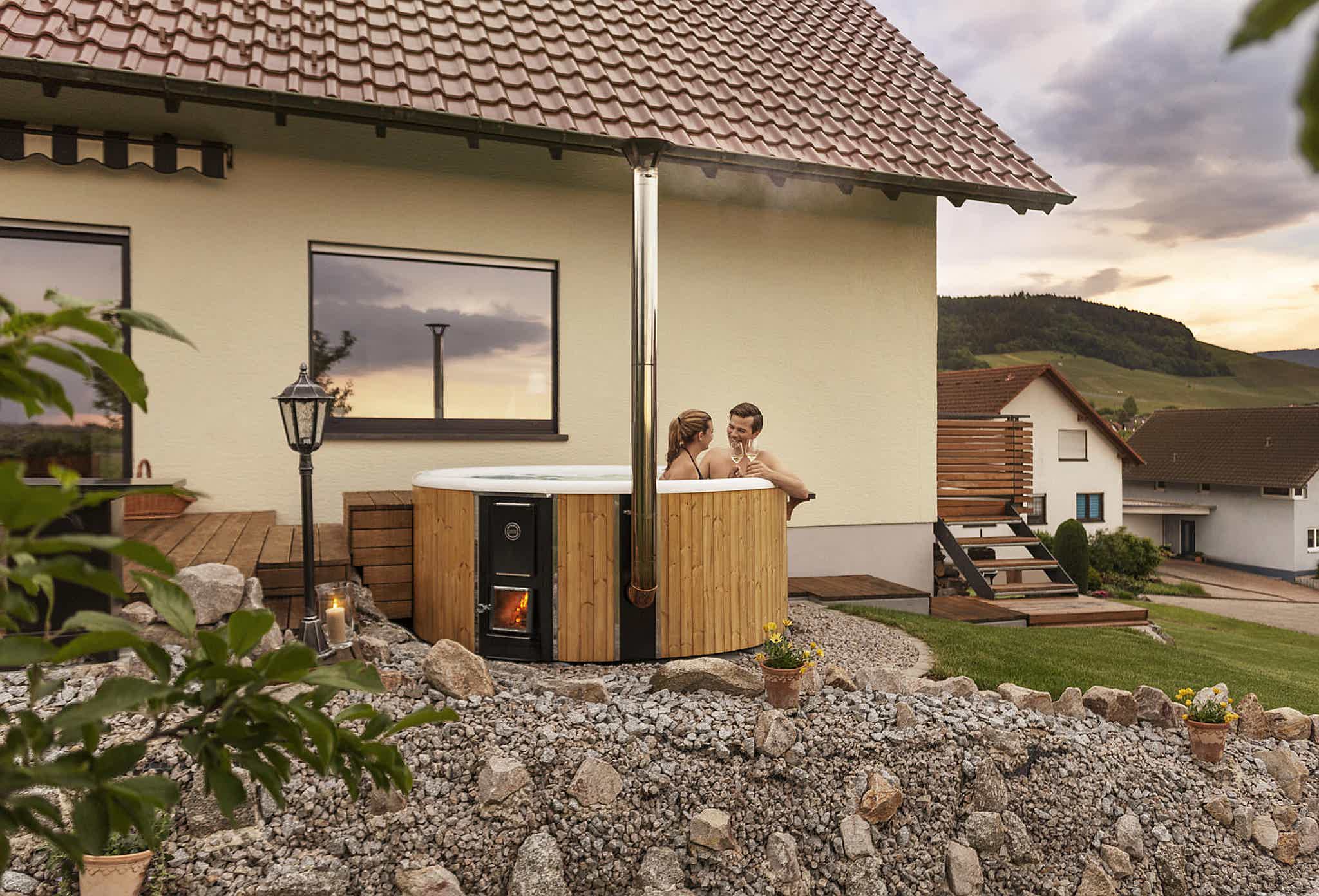 Frauke and Markus relaxing in their Skargards Regal DualBurn 220 hot tub, with their house and garden in the background.