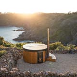 Luxurious hot tub on a rocky hillside with a wooden exterior and fireplace, offering a serene outdoor experience.