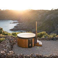 Luxurious hot tub on a rocky hillside with a wooden exterior and fireplace, offering a serene outdoor experience.