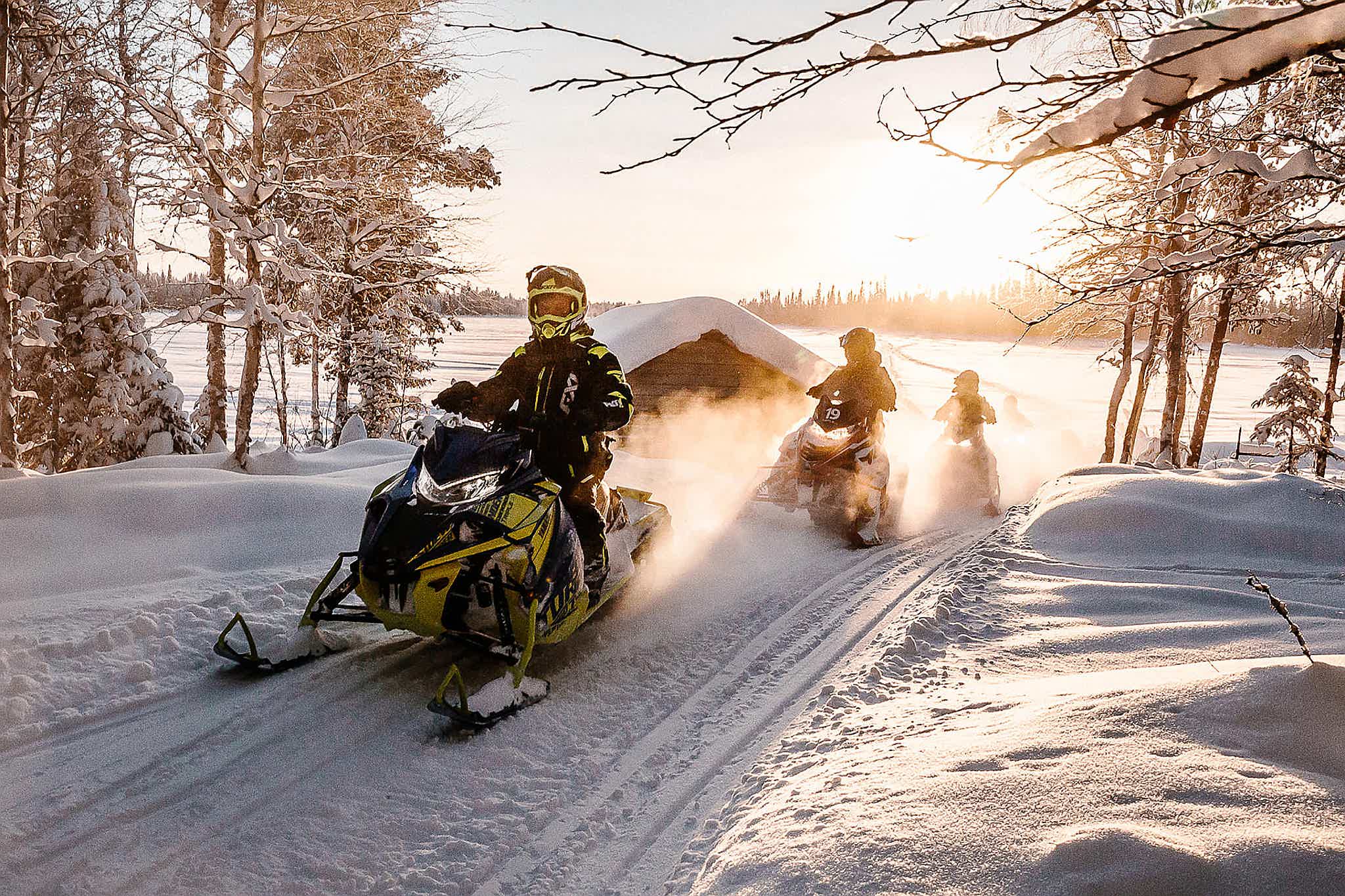 People on snowmobiles in a snowy Swedish landscape at sunset.