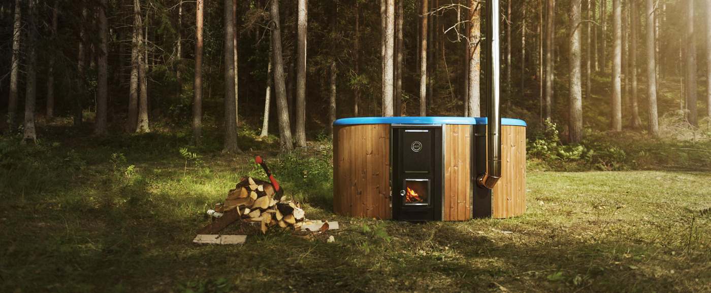 Skargards Regal in nature The Skargards Regal wood-burning hot tub with the blue vat placed next to a pile of wood in the Swedish nature.