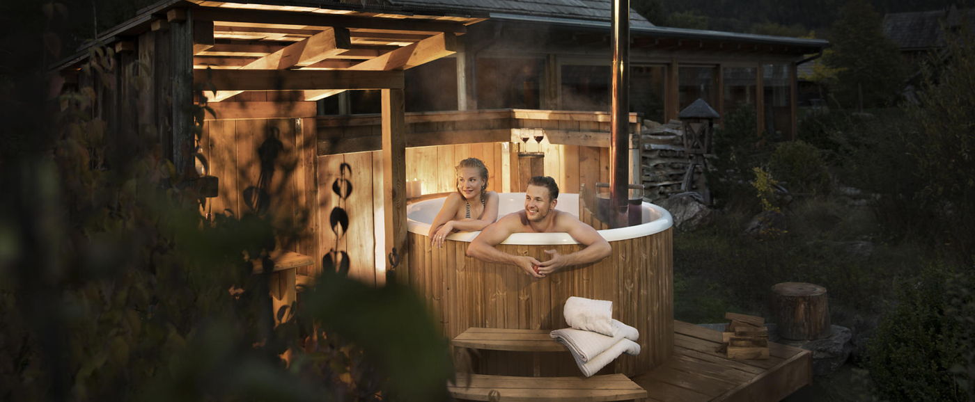 Night picture of the wooden hot tub Skargards Panel with a couple inside at Landgut Moserhof